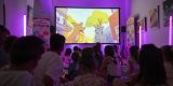 Niños y niñas sentados en el suelo participando en un debate con la mediadora Vicki Dos Santos en el Centro Sociocultural de La Graciosa.