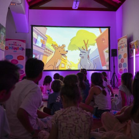 Niños y niñas sentados en el suelo participando en un debate con la mediadora Vicki Dos Santos en el Centro Sociocultural de La Graciosa.