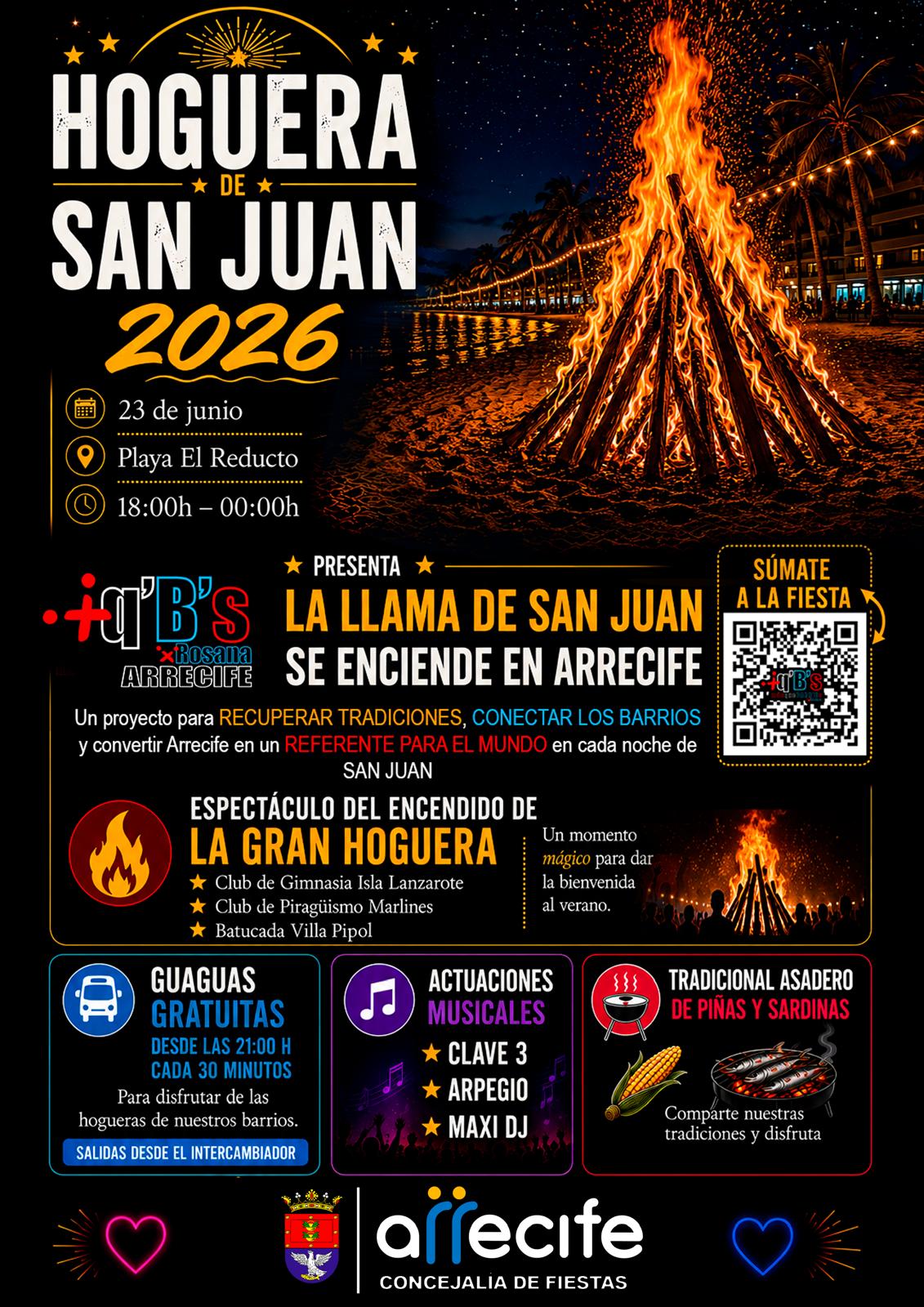 Gran hoguera encendida de noche en la arena de la playa de El Reducto con el mar y luces de Arrecife al fondo.