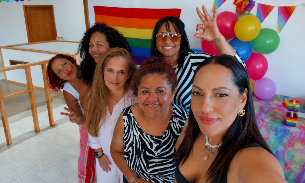 Asistentes de todas las edades sonriendo y pintando juntos un cartel conmemorativo con los colores de la bandera del Orgullo LGTBIQ+.
