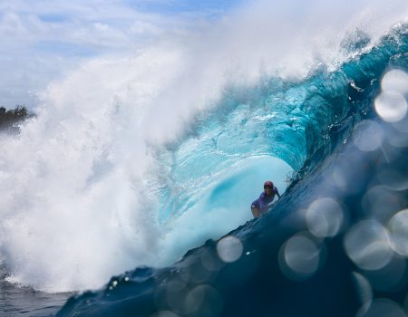 Primer plano de la fotógrafa marina Christa Funk nadando entre grandes olas con su cámara de agua en Hawái.