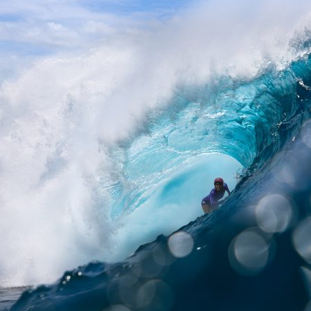 Primer plano de la fotógrafa marina Christa Funk nadando entre grandes olas con su cámara de agua en Hawái.